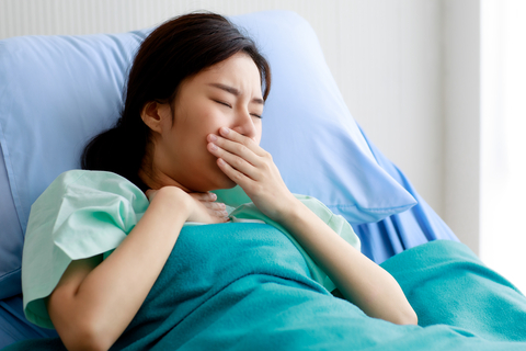 Young Asian woman coughing in hospital bed