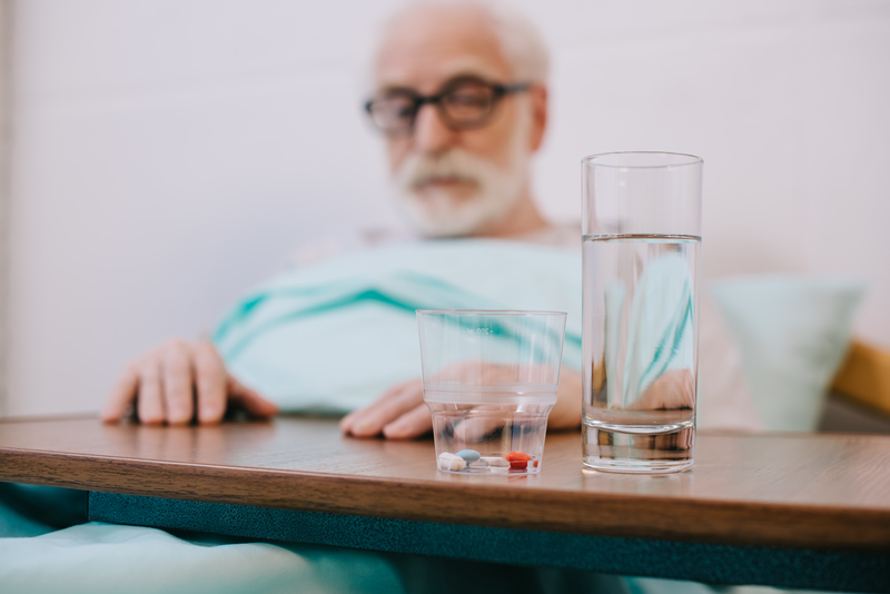 Senior man in hospital with pills and glass of water